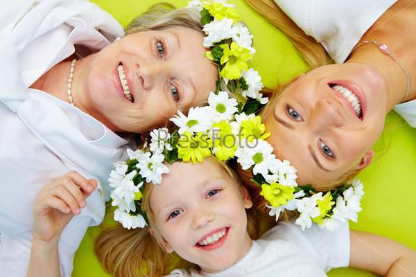 Portrait of grandmother, mother, girl with flowers lying on green floor