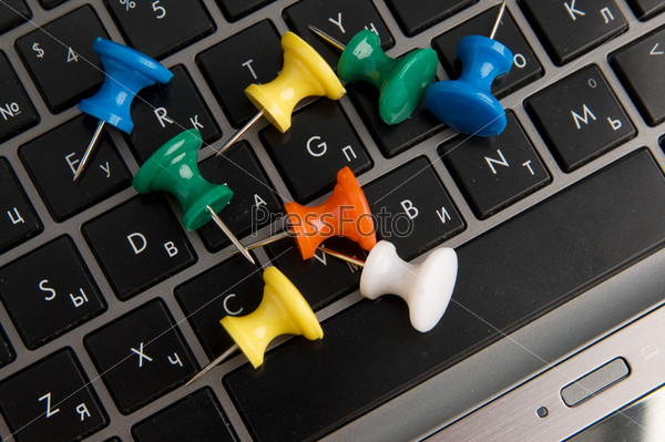 Several many-colored thumbtacks and keyboard of laptop
