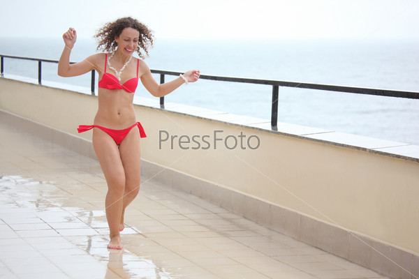 beauty girl runs on veranda near sea under rain