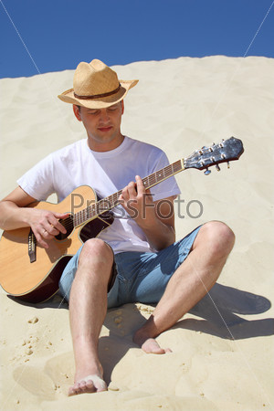 guy in straw hat plays guitar sitting on sand