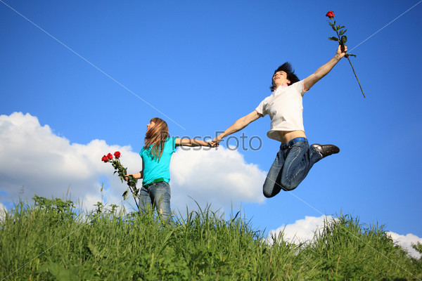 guy with rose jumps holding girl with roses by hand