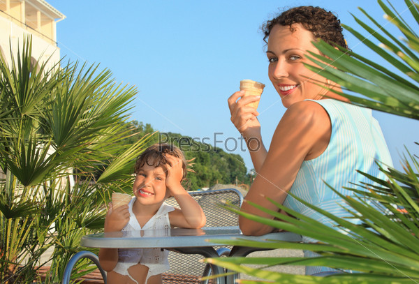 little girl and young woman eat ice-cream near palm trees on resort