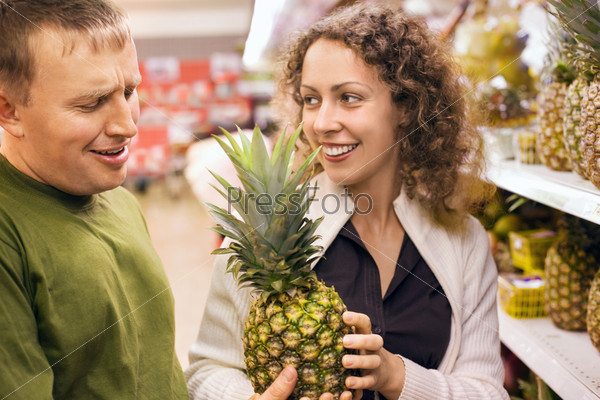 Smiling young man and woman buy pineapple in supermarket