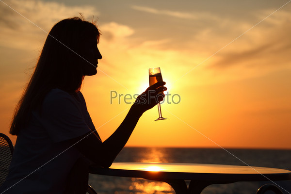 Female silhouette on sunset at  table with  glass in hand