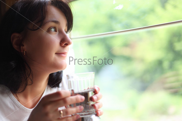young woman holds glass and looks in train`s window