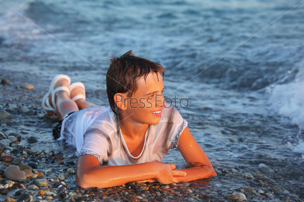 teenager boy in wet clothes lying on stones on seacoast