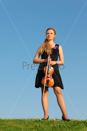Girl with violin stands on grass against sky