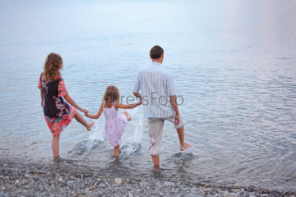 Happy family with little girl go in water, standing back