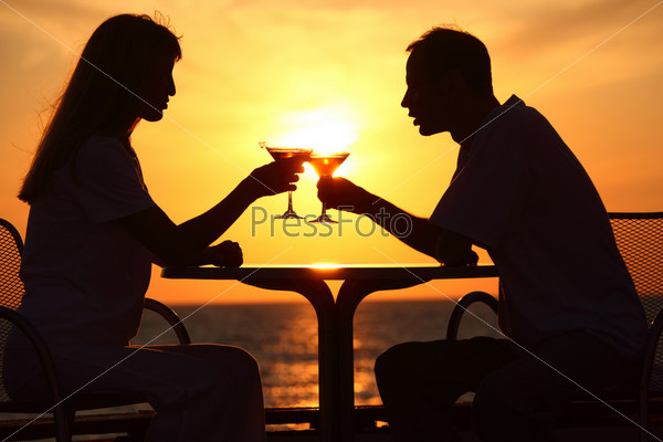 man and woman clink glasses on sunset outside
