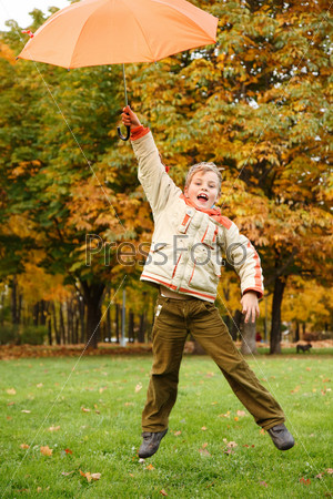 Cheerful boy in autumn park. Has jumped with orange umbrella over head.