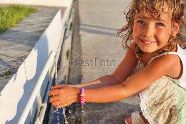 Smiling little girl washes hands water from pipe in street
