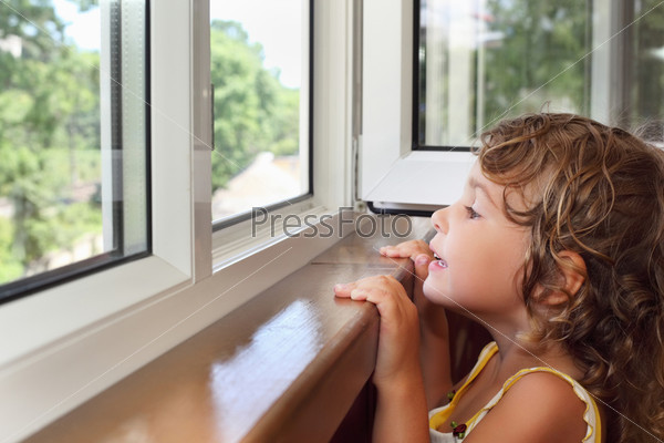 Pretty smiling little girl on balcony, look from window