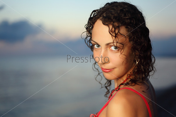 Curly beautiful young woman near sea in evening, Steadfastly looking