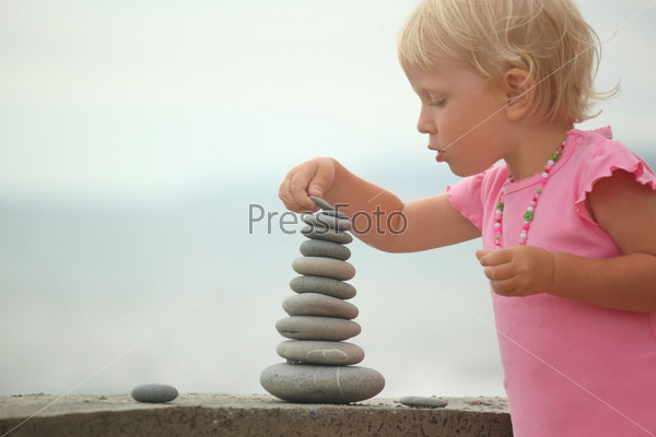 little girl wearing pink dress is building a construction from pebble stones. focus on top of construction