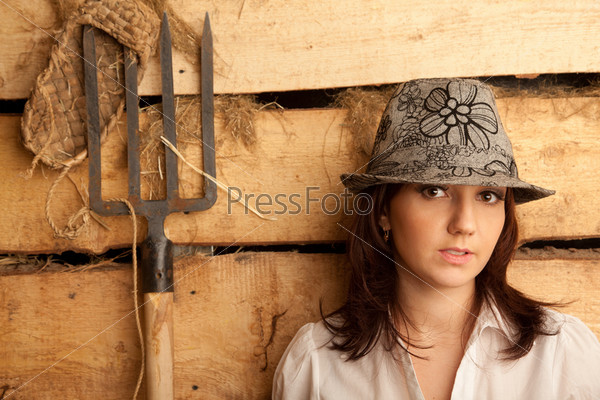 Portrait of girl in hat in hayloft with pitchfork and bast shoes. Horizontal format.