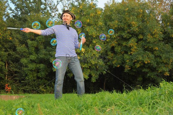 man with drawed beard and whiskers in pirate suit is blowing soap bubbles.