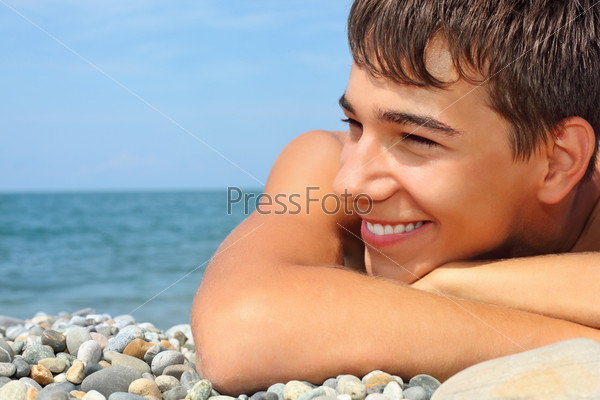 teenager boy lying on stony seacoast, looking afar