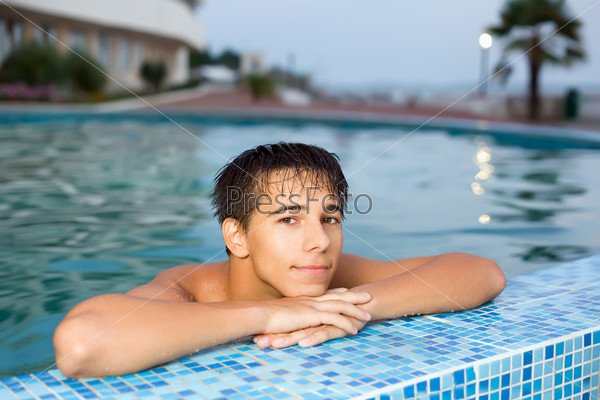 teenager boy relaxing near ledge in pool open-air, looking at camera