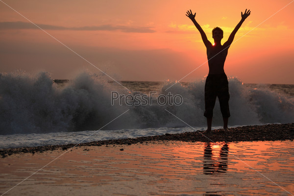 Silhouette guy lifted hands upwards on sunset wavy beach