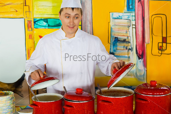 cheerful cook in uniform near red pans in public catering restaurant