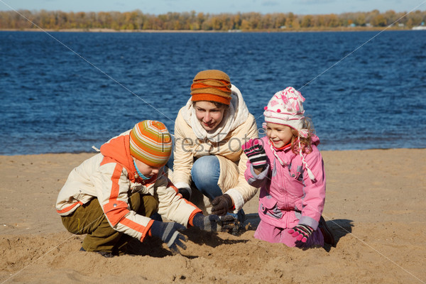 Boy and girl with mum play beach on river bank in autumn day.