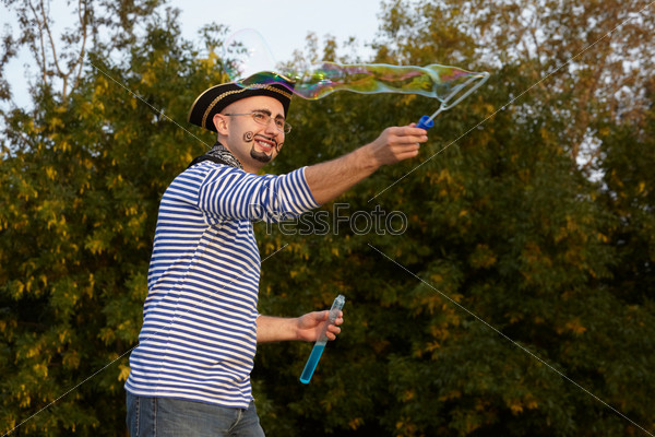 joyful man with drawed beard and whiskers in pirate suit is blowing soap bubbles.