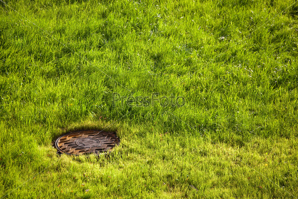 water drain metal rusty hatch on green grass field. water drain drainpipe system