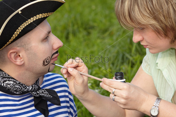 woman drawing funny whiskers and beard on man\'s face