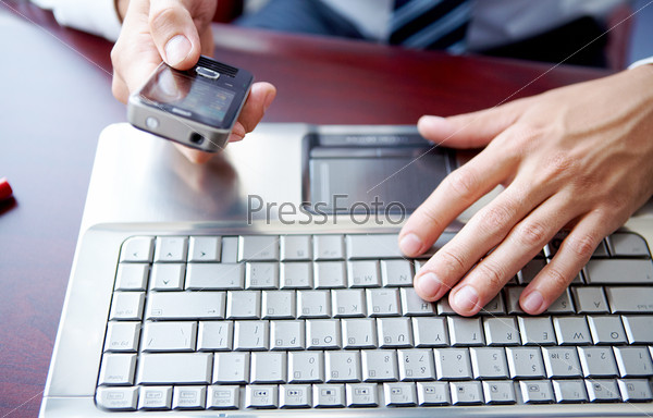 Close up image of male hands working on laptop and cell phone