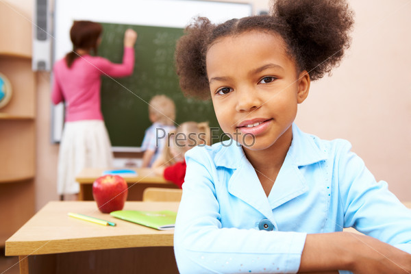 Portrait of smart schoolgirl smiling at camera during lesson in classroom