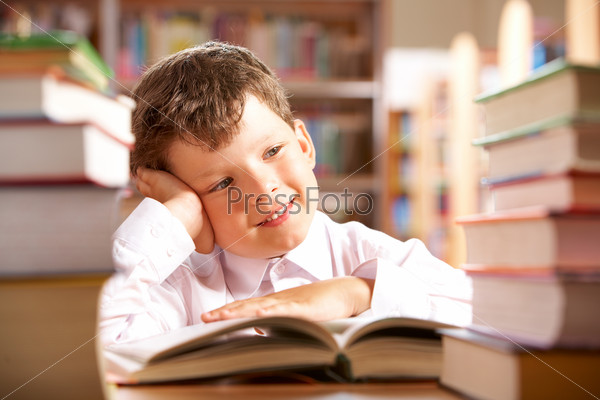 Мечтающий мальчик с книгами в библиотеке