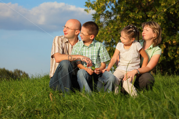 dad, mom, son and daughter in early fall park. they sitting on grass and looking at sunset