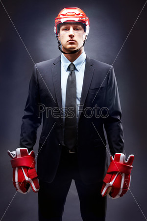 Portrait of young businessman in suit and hockey helmet and gloves