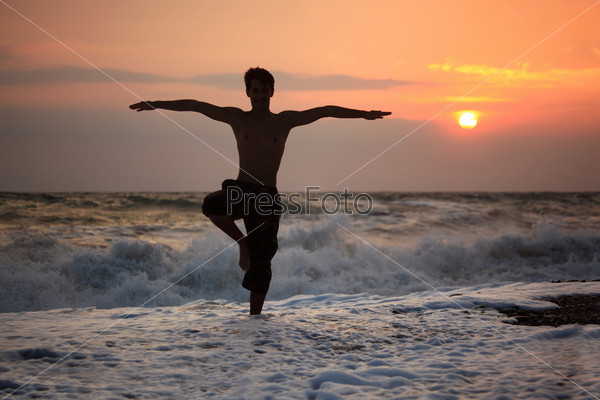 Silhouette guy yoga on sunset wavy beach