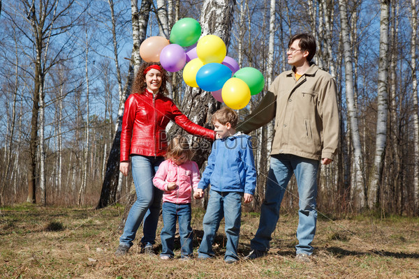 Parents with the daughter and the son walk in park with balloons.