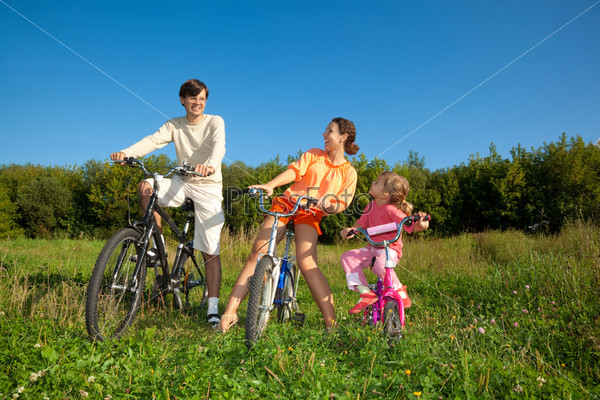 Семья из трех человек на велосипедах в парке в солнечный день
