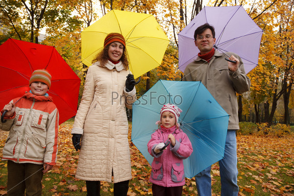 Family from four persons in autumn park with multi colored umbrellas.