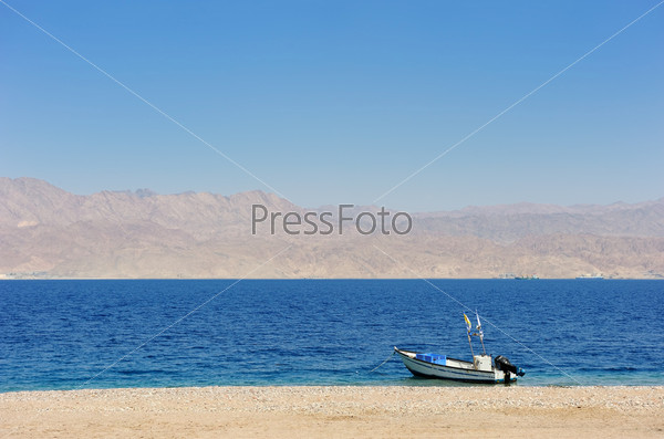 Gulf of Eilat Red Sea, the boat on the shore and Jordanian mountains in the background.