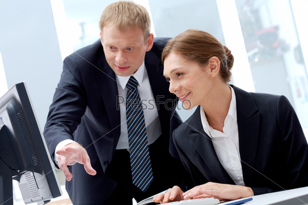 Successful businessman explaining something to his pretty colleague while they looking at monitor