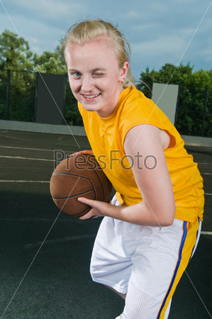 Cheerful winking teenage girl with basketball wearing yellow