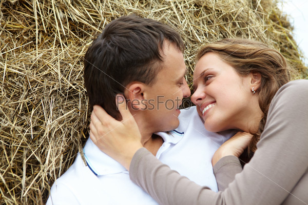Photo of affectionate couple looking at each other while lying on haystack