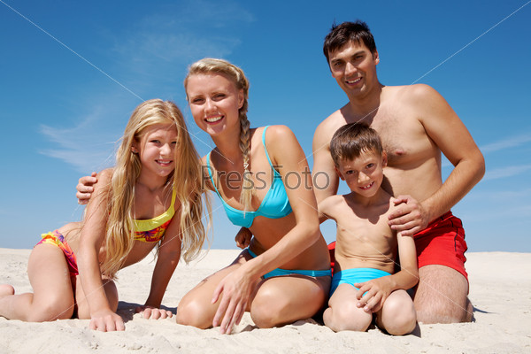 Photo of happy family sitting on sand on summer vacation