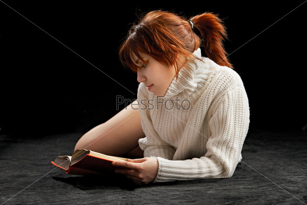Молодая девушка читает книгу, лежа на полу
