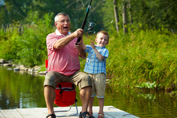 Photo of grandfather and grandson throwing fishing tackle in natural environment