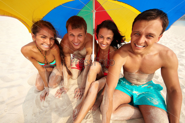 Компания молодых людей на пляже под зонтом