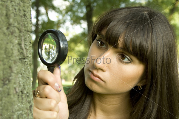 Young woman is interested in beautiful things a little bit of life. He looks through a magnifying glass on the bark of a tree