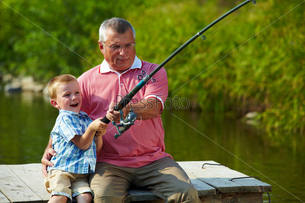 Photo of grandfather and grandson pulling rod while fishing on weekend, stock photo