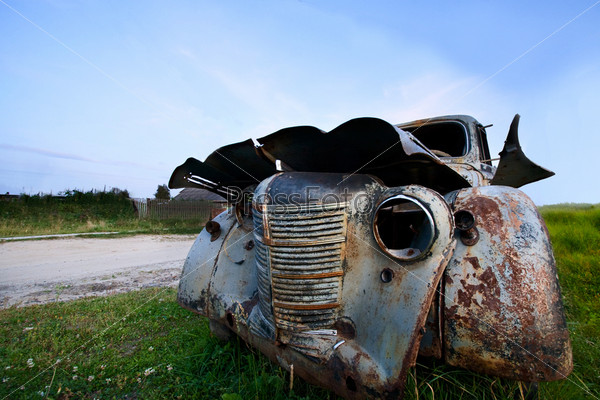 A wide angle view of a rusty old abandoned car under blue skies, stock photo