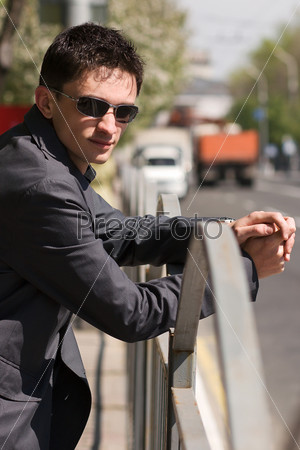 Young guy in black sunglasses waiting for someone near the road in the middle of a day