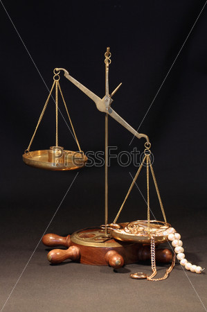 Old brass weight scale with various jewelry on dark background